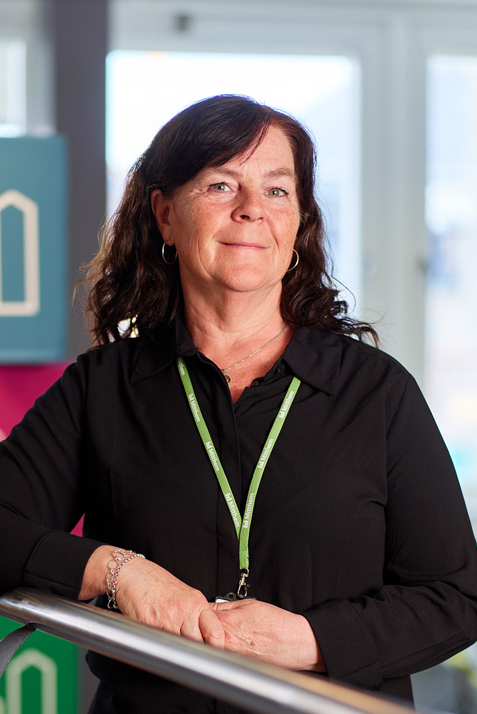Jeanette står lutad vid ett trappräcke och ler. Bild.