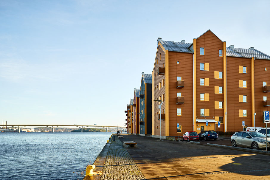 De bruna trähusen i Inre Hamnen ligger precis vis vattnet, men Sundsvallsbron i bakgrunden. Bild.